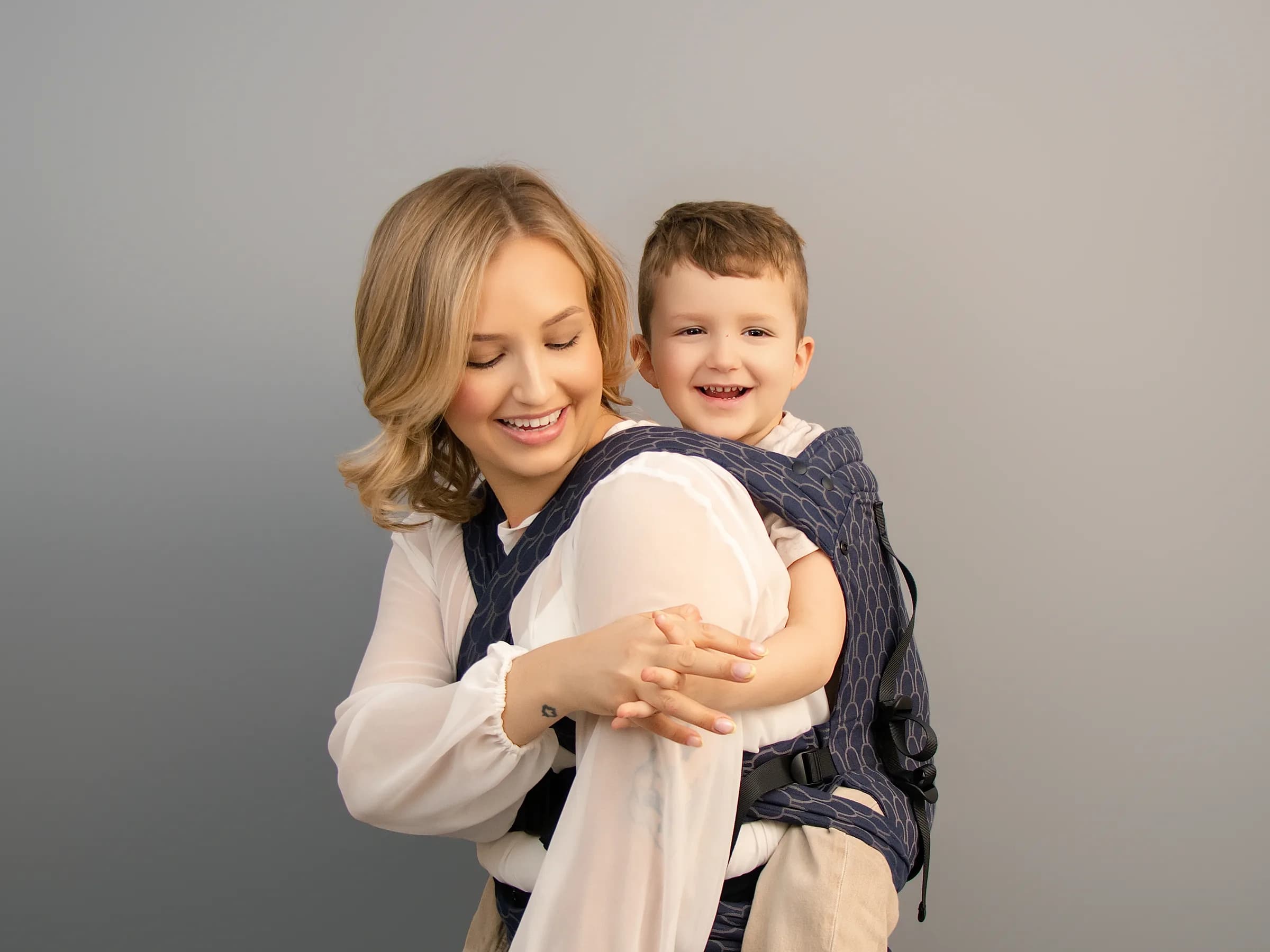 A parent hip-carrying her big kid in a Babue carrier